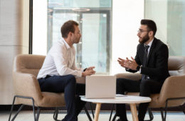 Middle eastern and caucasian ethnicity businessmen seated on armchair in modern office talking solve common issues, banker telling to client regarding bank services make recommendations and consulting